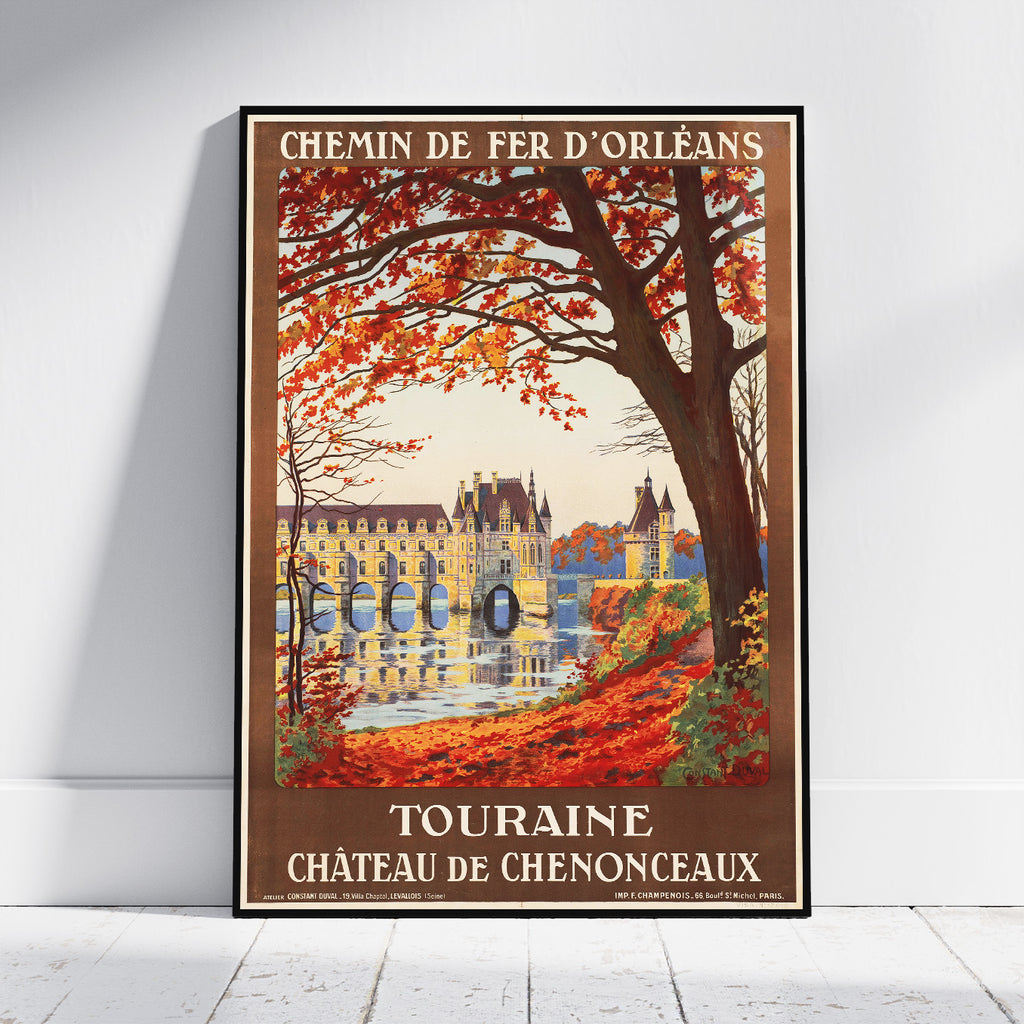 A framed vintage-style travel poster leaning against a white wall on a light wood floor. The poster reads “CHEMIN DE FER D'ORLÉANS” at the top and “TOURAINE À CHÂTEAU DE CHENONCEAUX” at the bottom, showing an autumn scene with orange-red leaves, a large tree, and a yellow chateau by the water.