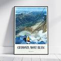 A framed vintage-style travel poster leaning against a white wall on a light floor. The poster shows a mountain valley with snow, a gondola, and the text 'CHAMONIX-MONT BLANC' and 'FRANCE'.