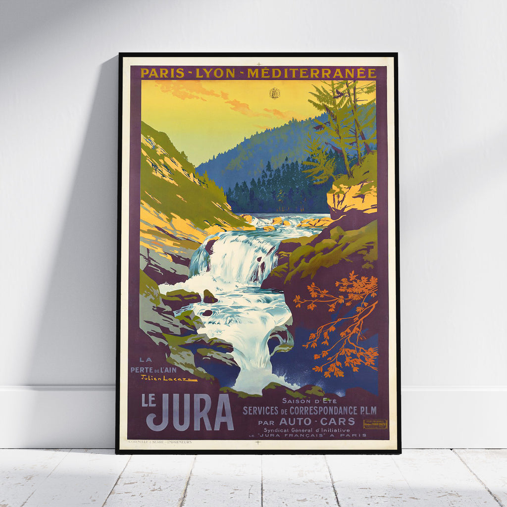 A framed vintage-style travel poster leaning against a white wall on a light wood floor. The poster depicts a scenic waterfall in the Jura mountains with bold retro typography reading 'PARIS - LYON - MEDITERRANEE' at the top and 'LE JURA' at the bottom.