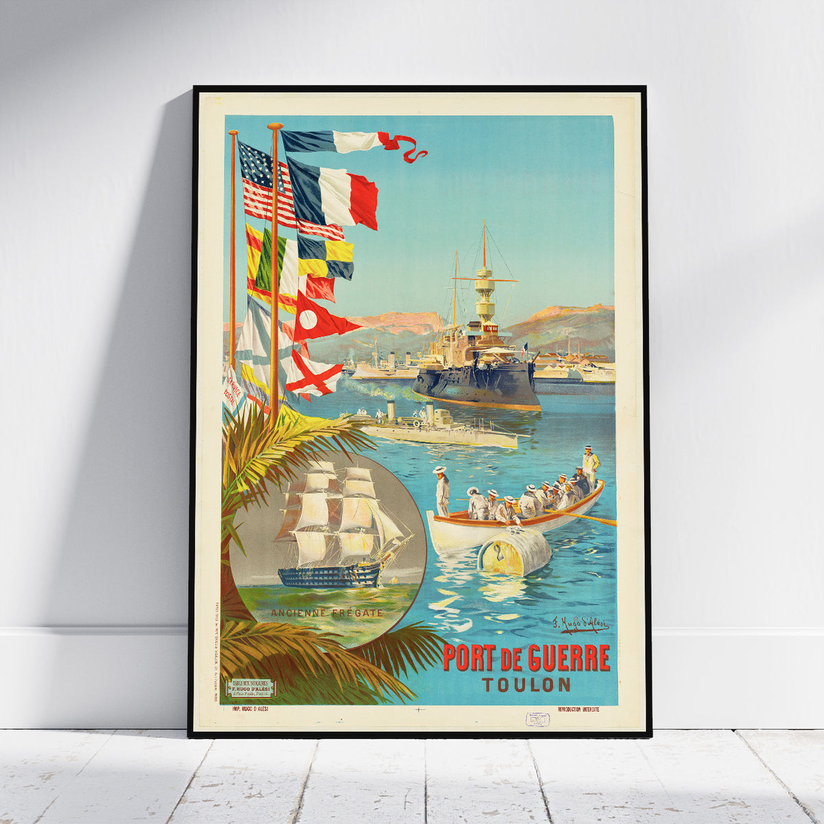 A framed vintage travel poster leaning against a white wall on a light wood floor. The poster depicts a coastal harbor scene with ships, palm leaves, multiple national flags, and the text 'PORT DE GUERRE TOULON' in red at the bottom.