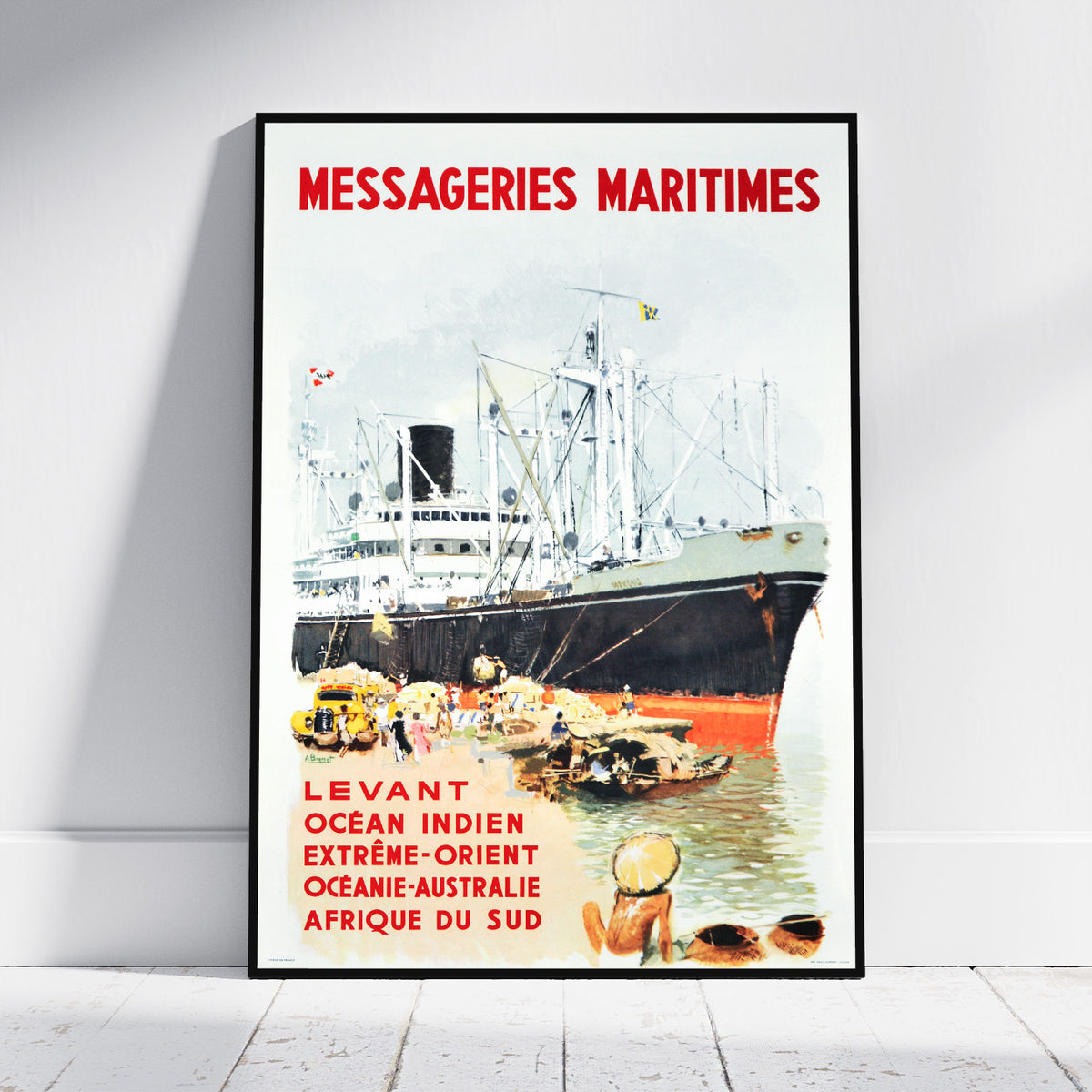 A framed vintage-style shipping poster leaning against a white wall on a light wood floor. The poster features the text 'MESSAGERIES MARITIMES' in red at the top and additional red text near the bottom, with an illustration of a large ocean liner docked at a harbor and small boats in the foreground.