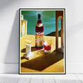 A framed vintage-style poster leaning against a white wall on a light wood floor. The artwork shows a bottle of Cinzano Bitter and a glass of red drink on a sunlit table, with a teal sky and dark hills in the background.