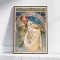 A framed Art Nouveau style poster leaning against a white wall on a light wood floor. The poster features an illustrated seated woman in a cream gown with red floral accents, blue circular background details, and the text 'PRINCESS PACIA' at the top.