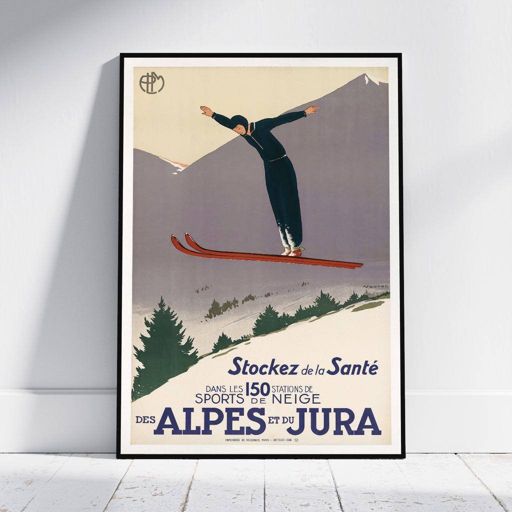 A framed vintage-style travel poster leaning against a white wall on a light floor. The poster shows a skier in midair over snowy mountains, with French text reading 'Stockez de la Santé DANS LES 150 STATIONS DE SPORTS DE NEIGE DES ALPES ET DU JURA.
