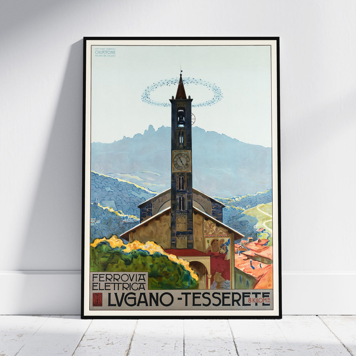 A framed vintage-style travel poster leaning against a white wall on a light wood floor. The artwork shows a church tower in a mountain village with the text 'FERROVIA ELETTRICA LVGANO - TESSERETE' and a circular logo at the top left.