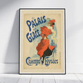 A framed vintage-style poster leaning against a white wall on a light floor. The poster shows an illustrated woman in a flowing red dress and hat with large blue text reading 'PALAIS DE GLACE' and 'Champs-Flyscées'.