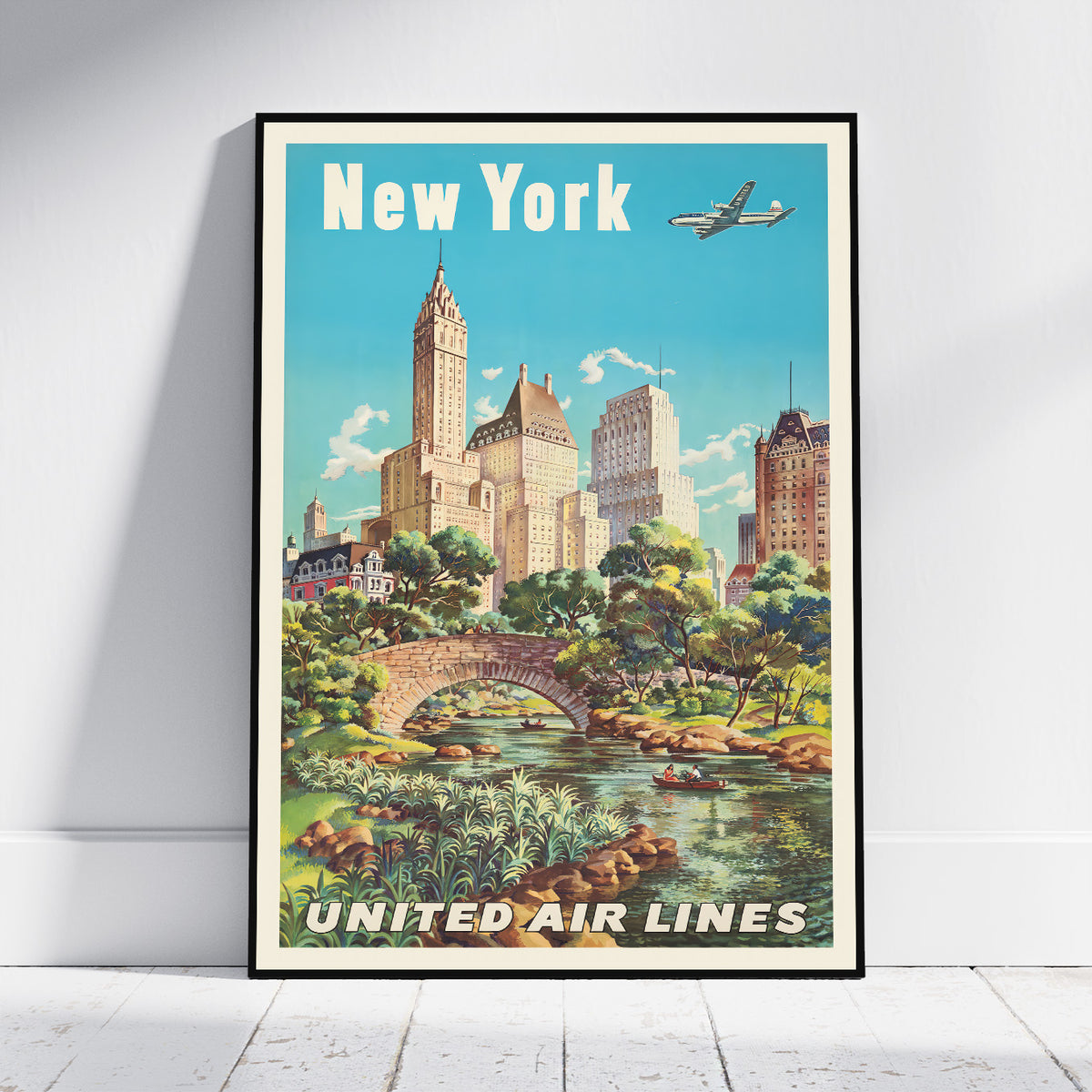A framed vintage-style New York City poster leaning against a white wall on a light floor. The poster shows the words 'New York' at the top and 'UNITED AIR LINES' at the bottom, with a retro illustration of skyscrapers, trees, a stone bridge, a river, and an airplane in the sky.