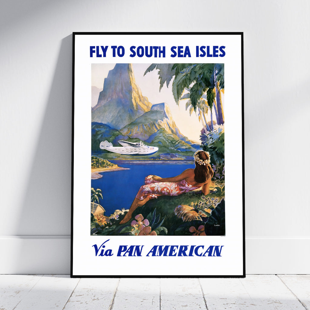 A framed vintage-style travel poster leaning against a white wall on a light floor. The poster reads 'FLY TO SOUTH SEA ISLES' at the top and 'Via PAN AMERICAN' at the bottom, with an illustrated tropical scene showing blue water, mountains, palm trees, and a woman reclining by the shore.
