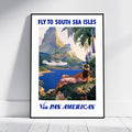 A framed vintage-style travel poster leaning against a white wall on a light floor. The poster reads 'FLY TO SOUTH SEA ISLES' at the top and 'Via PAN AMERICAN' at the bottom, with an illustrated tropical scene showing blue water, mountains, palm trees, and a woman reclining by the shore.