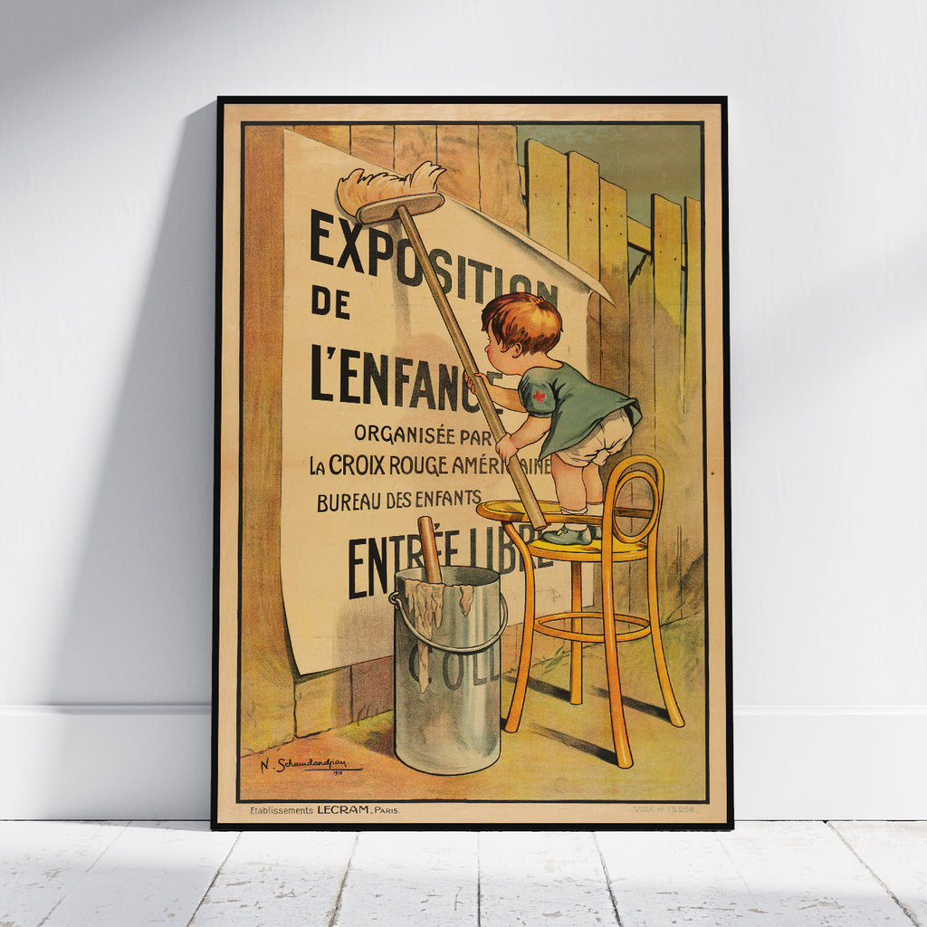 A framed vintage poster leaning against a white wall on a light wood floor. The poster shows an illustration of a child painting on a wall with large French text reading 'EXPOSITION DE L'ENFANC'.