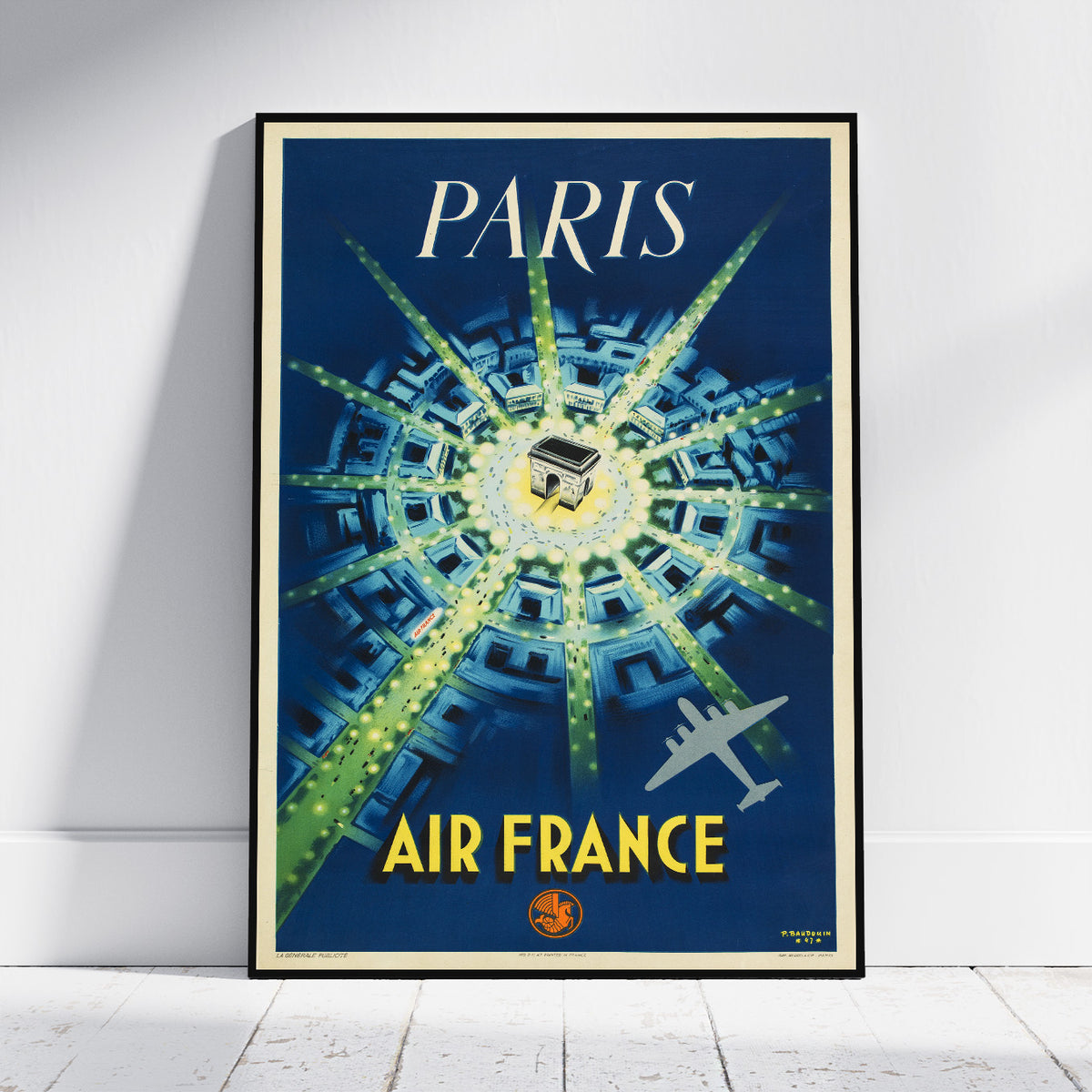 A framed vintage-style Paris Air France poster leaning against a white wall on a light floor. The poster features a deep blue background with a bright radial pattern in green and yellow, the word PARIS at the top, AIR FRANCE at the bottom, and an airplane illustration.