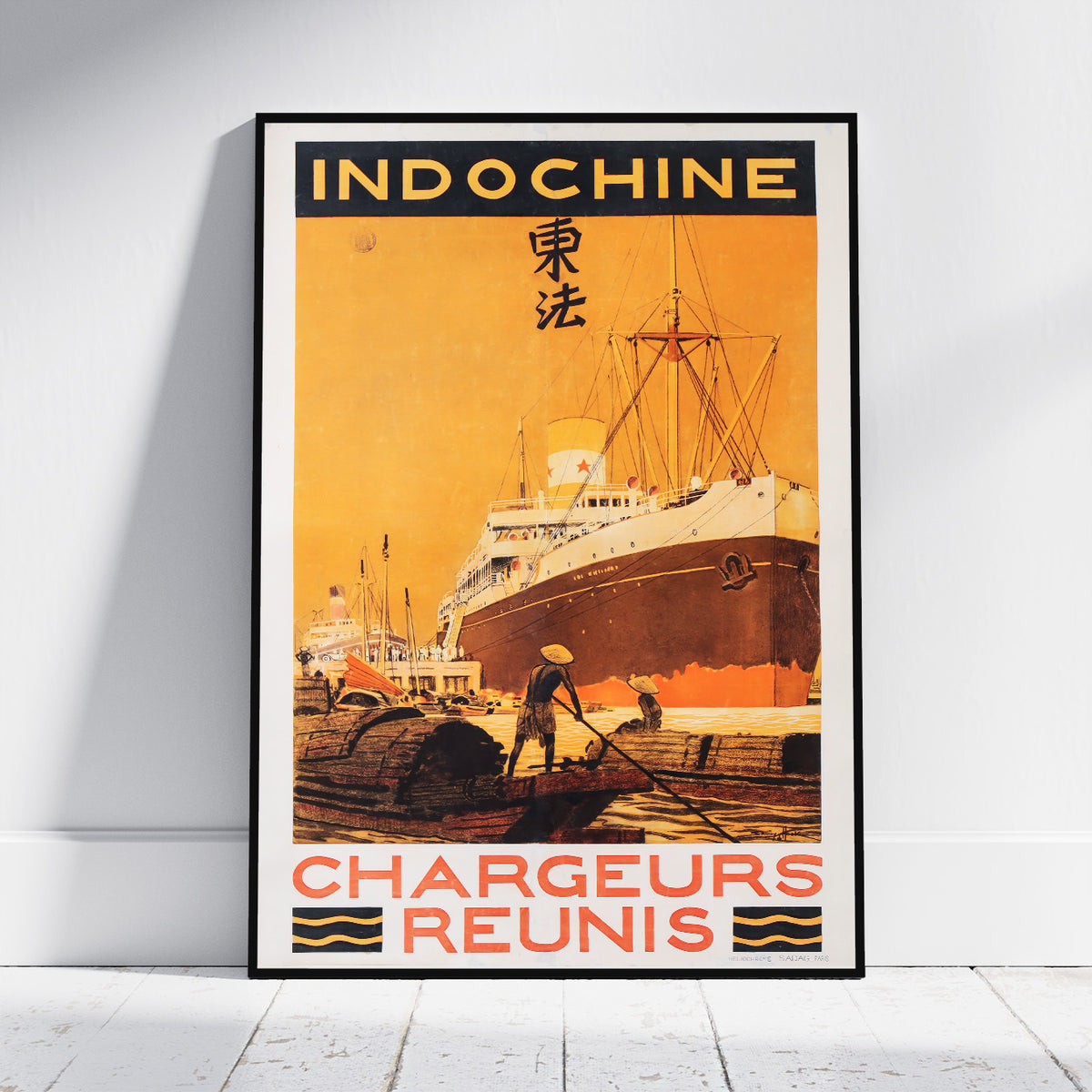 A framed vintage-style travel poster leaning against a white wall on a light floor. The poster reads "INDOCHINE" at the top and "CHARGEURS REUNIS" at the bottom, with an illustration of a large ship at a harbor in warm orange, yellow, and brown tones.