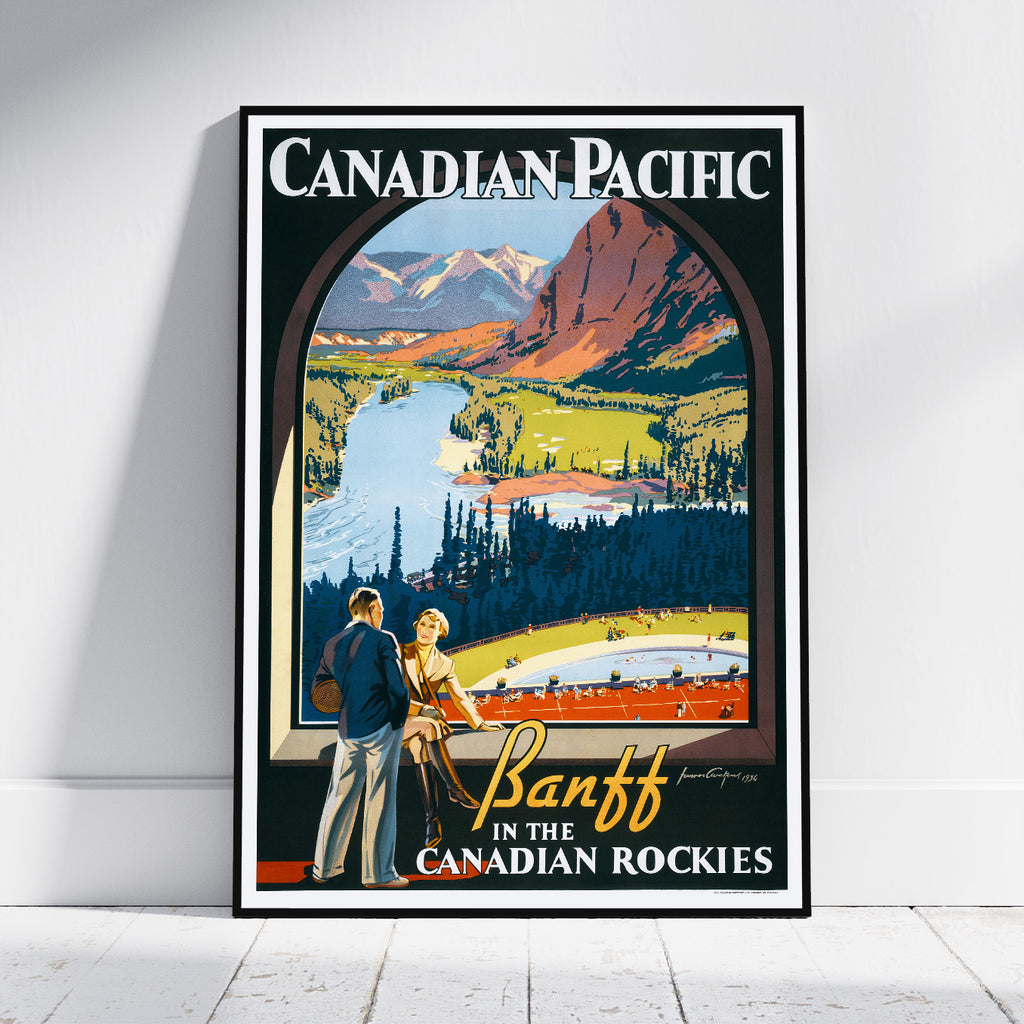 A framed vintage-style travel poster leaning against a white wall on a light floor. The poster reads 'Canadian Pacific' and shows a scenic mountain landscape with a river, trees, and two people standing in the foreground.