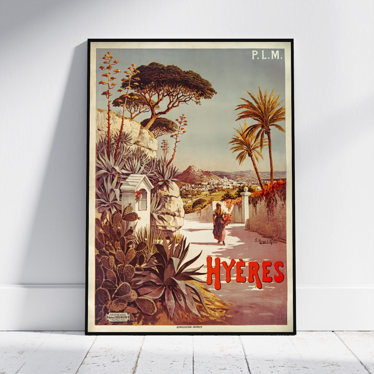 A framed vintage travel poster of Hyeres, Greece, leaning against a white wall on a light wood floor. The poster features a retro illustration of a Mediterranean coastal town with palm trees, cacti, and a figure walking along a path, with 'P.