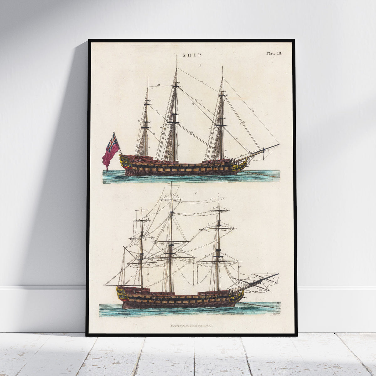 A framed vintage nautical print showing two antique sailing ships on an aged cream background, leaning against a white wall on a light wood floor.