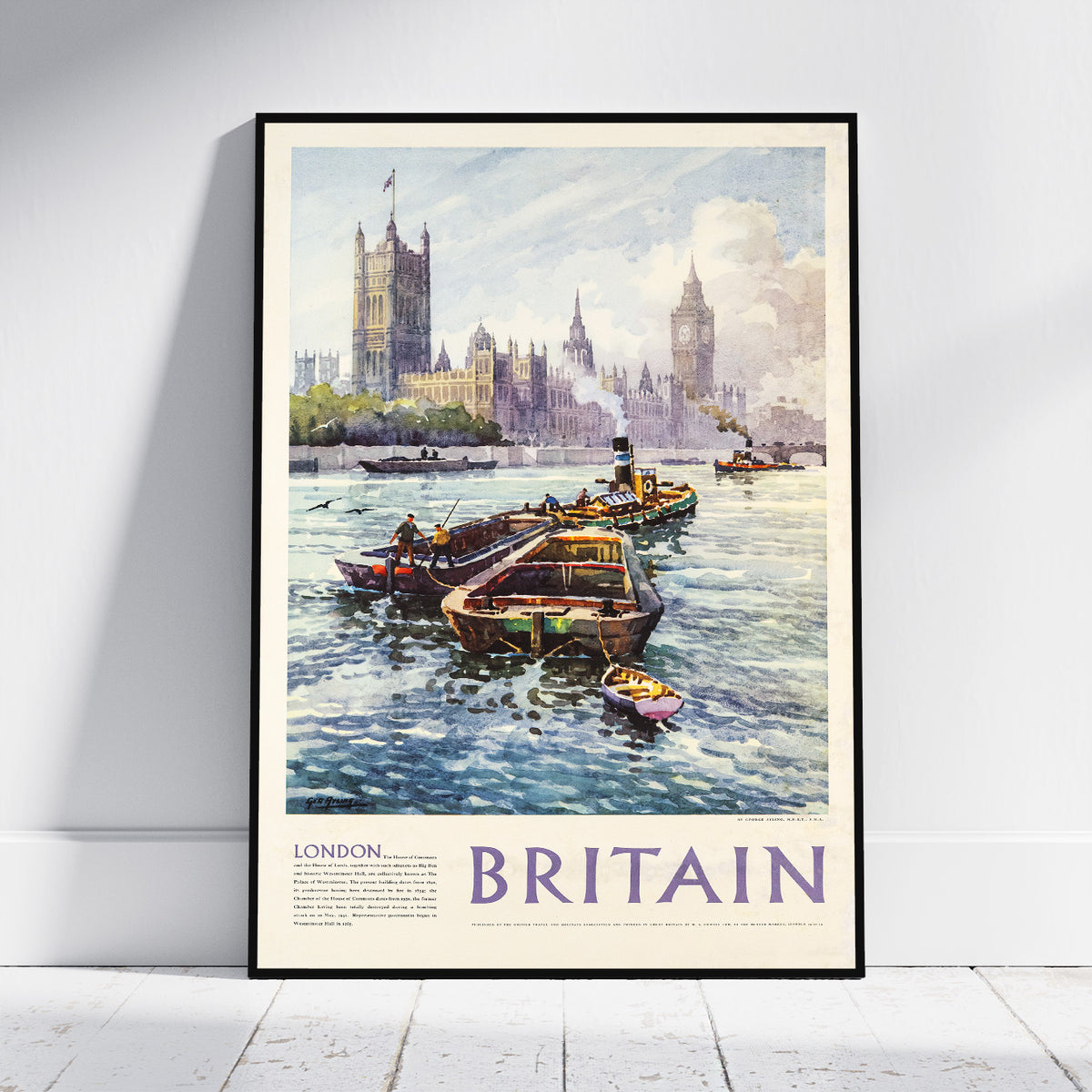 A framed vintage-style travel poster of London, Britain, leaning against a white wall on a light wood floor. The artwork shows boats on the River Thames with the Houses of Parliament and Big Ben in the background, and the word 'BRITAIN' printed prominently at the bottom.