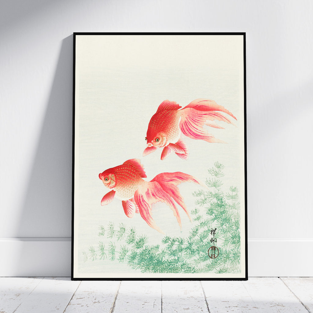 A framed art print featuring two red and orange goldfish swimming above green aquatic plants, displayed against a white wall on a light wood floor.