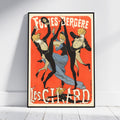 A framed vintage-style poster leaning against a white wall on a light floor. The poster features three dancing figures in black and beige costumes with a blue dress, set against a vivid red-orange background, with large cream text reading 'Foules Bergère' at the top and 'Les Citadins' at the bottom.