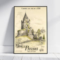 A framed vintage travel poster leaning against a white wall on a light wood floor. The poster features an illustration of a stone castle and historic town with French text reading 'CHEMINS DE FER DE L'EST' and 'Provins Tour de César'.