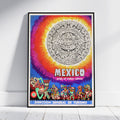 A framed poster featuring a colorful Mexican-themed design with a large Aztec calendar motif, rainbow gradient background, and illustrated figures along the bottom. The poster is displayed leaning against a white wall on a light wood floor.
