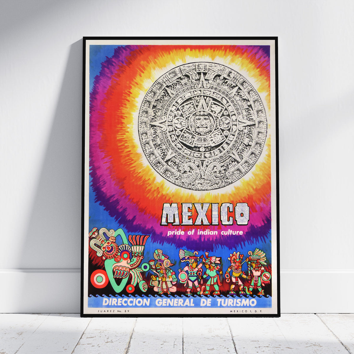 A framed poster featuring a colorful Mexican-themed design with a large Aztec calendar motif, rainbow gradient background, and illustrated figures along the bottom. The poster is displayed leaning against a white wall on a light wood floor.