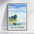 A framed vintage travel poster for 'Val de Loire' leaning against a white wall on a light wood floor. The watercolor-style print features a blue sky, white clouds, a sandy shore, green trees, and a small house, with the text 'VAL DE LOIRE' and 'SOCIETE NATIONALE DES CHEMINS DE FER FRANCAIS' at the bottom.