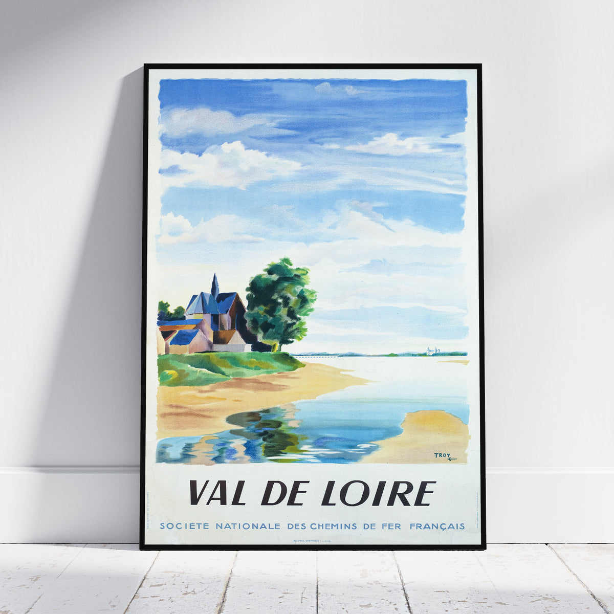 A framed vintage travel poster for 'Val de Loire' leaning against a white wall on a light wood floor. The watercolor-style print features a blue sky, white clouds, a sandy shore, green trees, and a small house, with the text 'VAL DE LOIRE' and 'SOCIETE NATIONALE DES CHEMINS DE FER FRANCAIS' at the bottom.