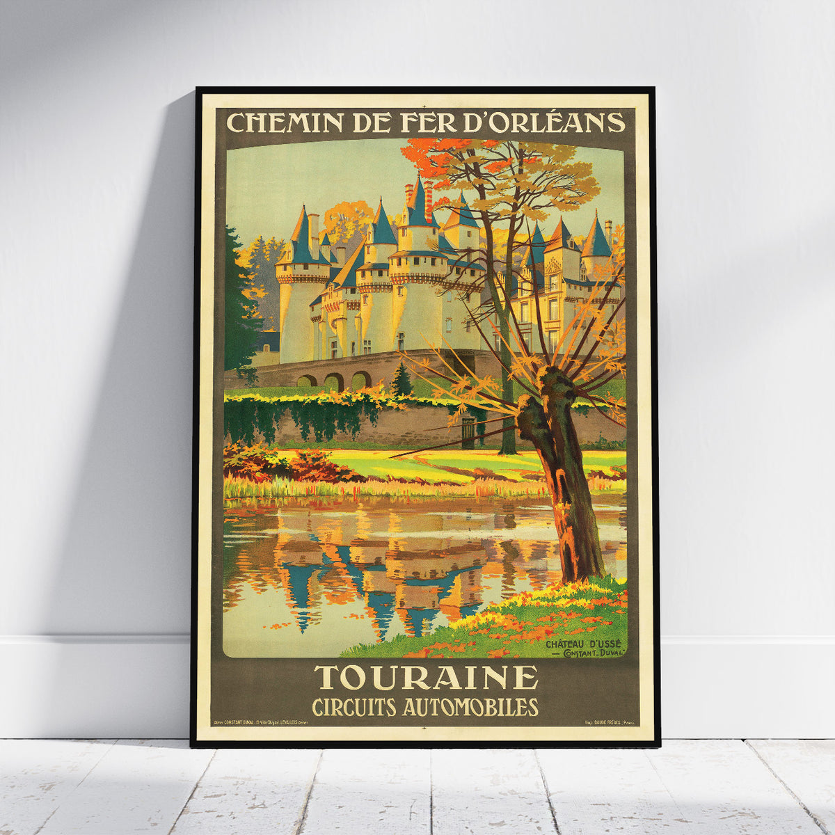 A framed vintage-style travel poster leaning against a white wall on a light wood floor. The poster shows a castle by a river with autumn trees and the text 'CHEMIN DE FER D'ORLÉANS' at the top and 'TOURAINE CIRCUITS AUTOMOBILES' at the bottom.