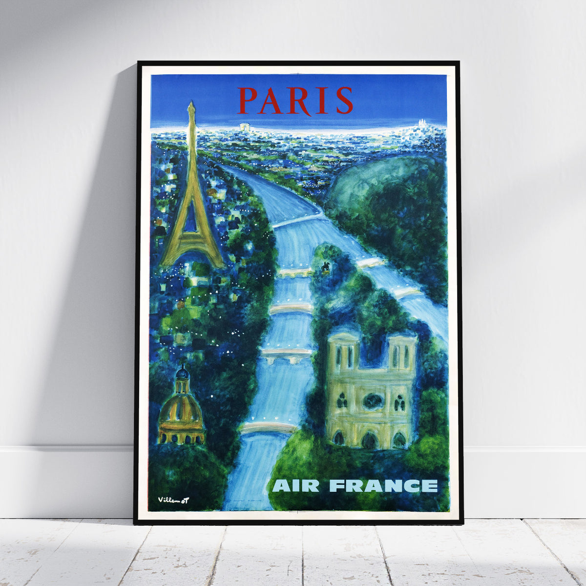 A framed vintage-style Paris travel poster leaning against a white wall on a light wood floor. The poster features the Eiffel Tower, a river winding through green cityscapes, and the words 'PARIS' at the top and 'AIR FRANCE' at the bottom.