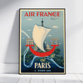 A framed vintage-style Air France poster leaning against a white wall on a light wood floor. The poster features a white sailboat, the Eiffel Tower, Paris landmarks, and the text 'AIR FRANCE' at the top and 'PARIS A 2000 ANS' at the bottom.