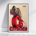 A framed vintage-style Citroón poster leaning against a white wall on a light floor. The artwork shows an old car above a large red 'C6' and 'CITROØN' text on a beige background, with 'SIX' in the upper right.
