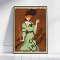 A framed vintage-style poster leaning against a white wall on a light wood floor. The poster features an illustrated woman in a light green dress holding a cigarette, with large French text reading 'Cachou Lajaunie' and additional text at the top and bottom.