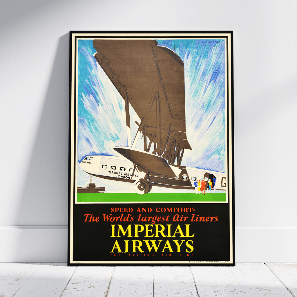 A framed vintage travel poster for Imperial Airways, leaning against a white wall on a light wood floor. The poster features an illustration of an early airplane and a large dirigible balloon, with bold text reading 'IMPERIAL AIRWAYS' and 'SPEED AND COMFORT'.