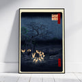 A framed Japanese-style art print leaning against a white wall on a light floor. The artwork depicts a dark night landscape with a large tree, glowing deer, and small red label details, enclosed in a black frame with a cream border.