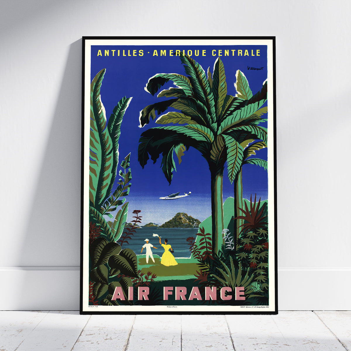 A framed vintage-style travel poster leaning against a white wall on a light floor. The poster shows tropical palm trees, a blue sky, a small airplane, and the text 'ANTILLES - AMERIQUE CENTRALE' at the top and 'AIR FRANCE' at the bottom.