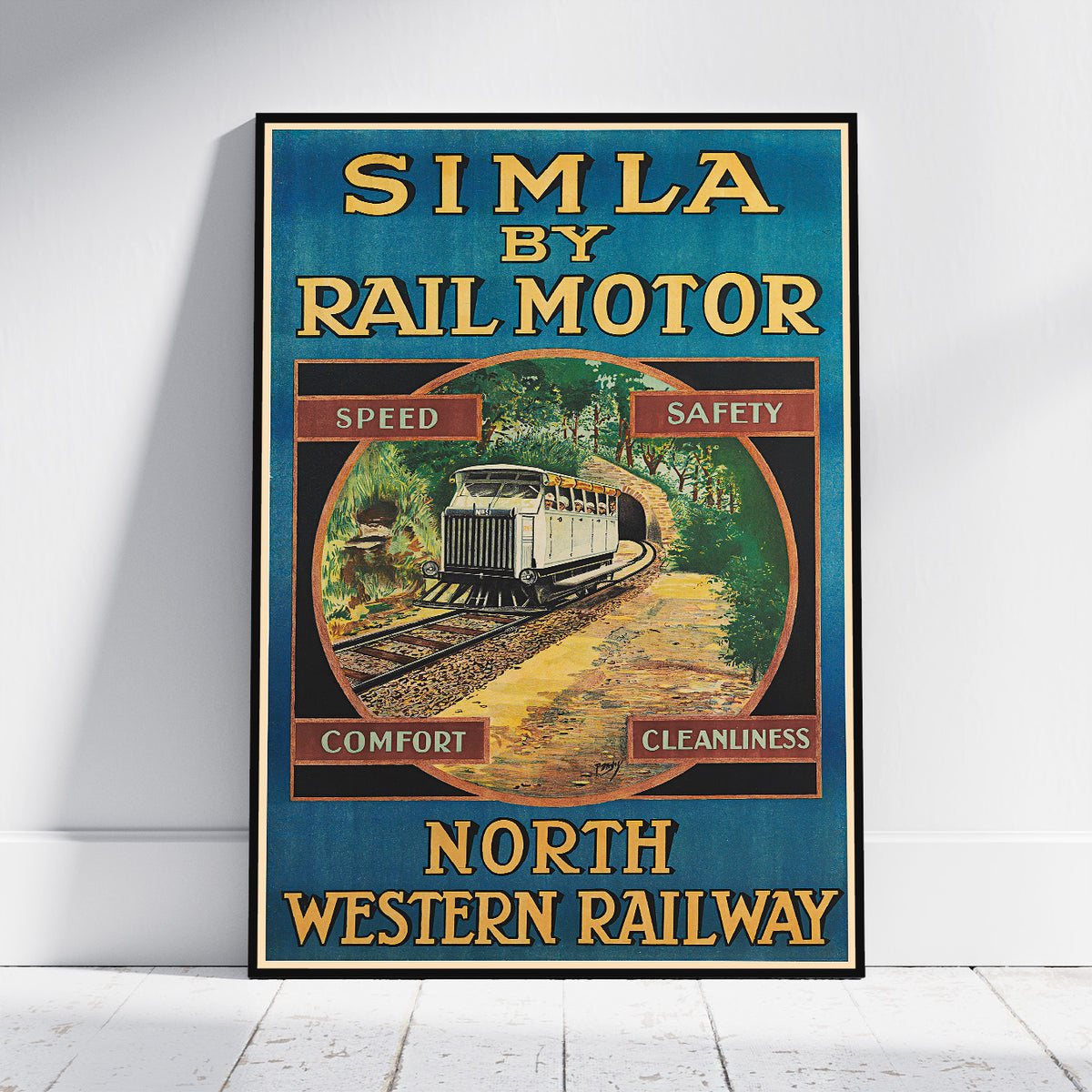 A framed vintage-style promotional poster leaning against a white wall on a light floor. The poster reads 'SIMLA BY RAIL MOTOR' and 'NORTH WESTERN RAILWAY,' with a train illustration and the words 'Speed,' 'Safety,' 'Comfort,' and 'Cleanliness.
