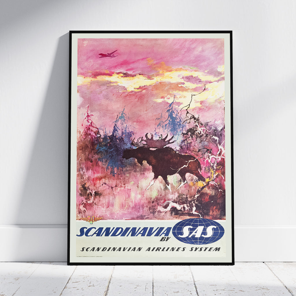 A framed vintage-style travel poster leaning against a white wall on a light floor. The artwork shows a moose in a snowy landscape under a pink and yellow sky, with the text 'SCANDINAVIA by SAS' and 'SCANDINAVIAN AIRLINES SYSTEM' at the bottom.