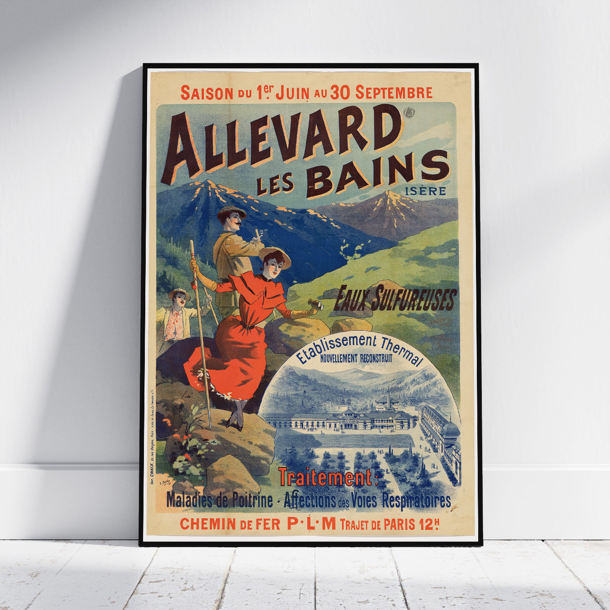 A framed vintage travel poster for Allevard Les Bains (Isere) is shown leaning against a white wall on a light wood floor. The poster features a colorful illustration of people in a red dress and a brown jacket against a mountain and thermal spa background.