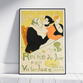 A framed vintage-style poster leaning against a white wall on a light wood floor. The poster features an Art Deco illustration of two people embracing, with one in a black suit and another in an orange dress, set against a yellow and cream background with French text reading 'Reine de Joie par Victor Jozze'.