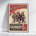A framed vintage French poster print leaning against a white wall on a light wood floor. The poster features illustrated figures in historical military clothing with bold red, black, beige, and blue text reading 'La Petite République Française' and 'Les Trois Mousquetaires'.