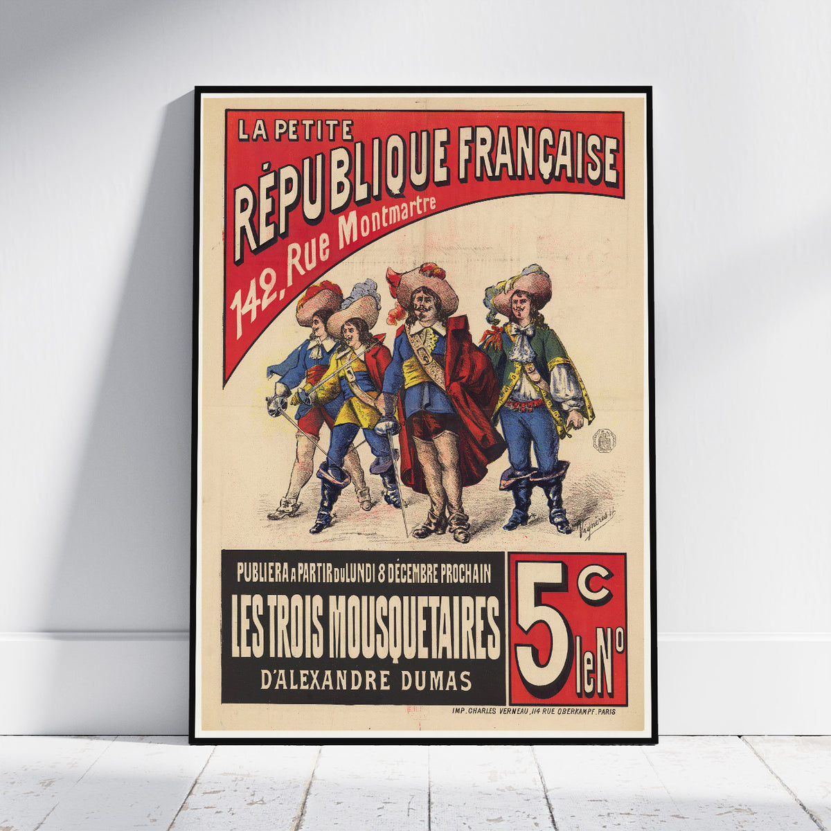 A framed vintage French poster print leaning against a white wall on a light wood floor. The poster features illustrated figures in historical military clothing with bold red, black, beige, and blue text reading 'La Petite République Française' and 'Les Trois Mousquetaires'.
