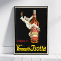 A framed vintage-style poster leaning against a white wall on a light wood floor. The poster features a black background with a large amber bottle labeled Vermouth Isotta and a white-clad figure reaching upward, with red and yellow text reading 'Evviva il Vermouth Isotta.