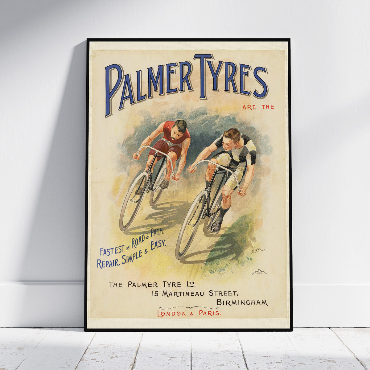 A framed vintage-style Palmer Tyres poster leaning against a white wall on a light wood floor. The poster shows two cyclists with large blue 'PALMER TYRES' lettering at the top and additional vintage text and branding.