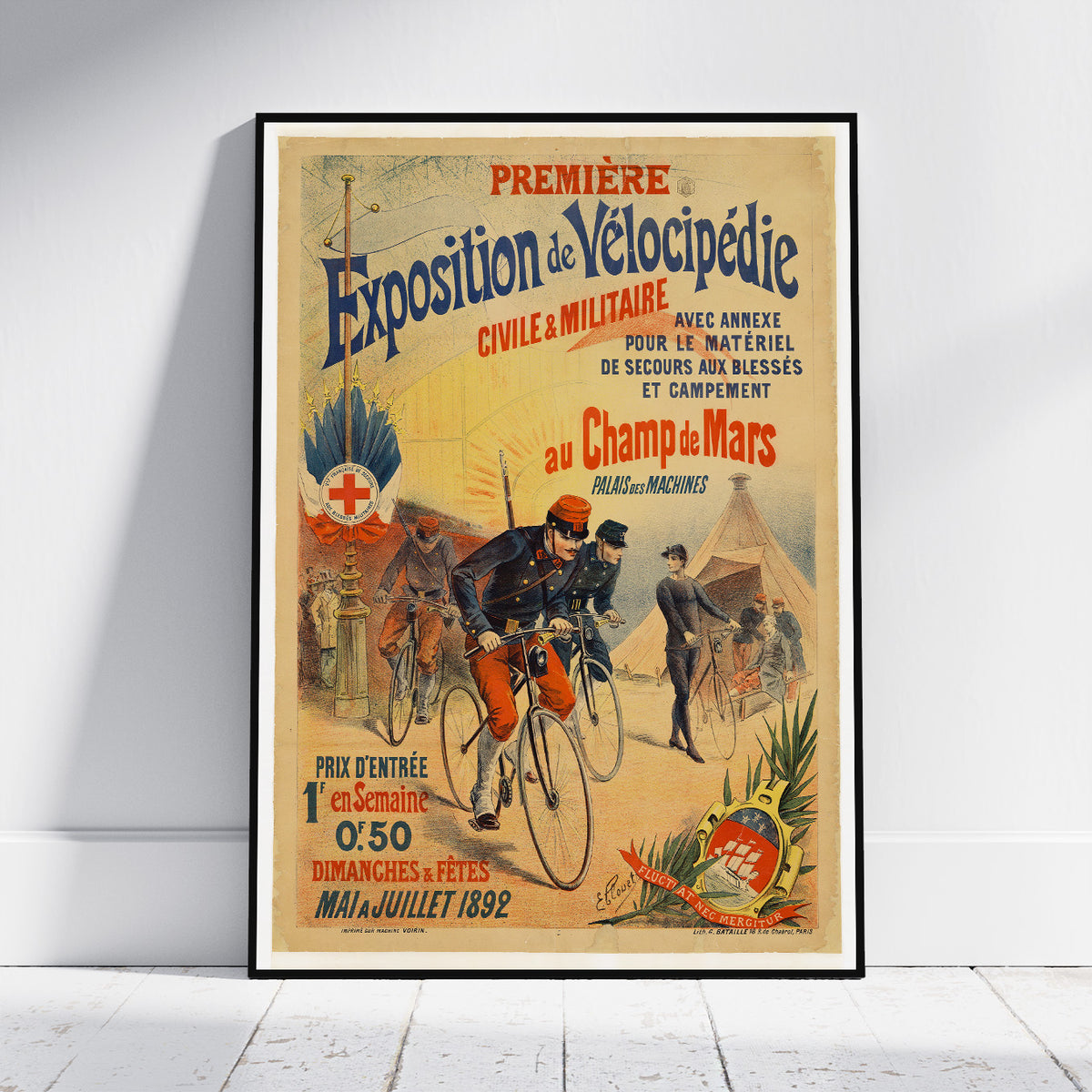 A framed vintage cycling poster leaning against a white wall on a light wood floor. The poster features colorful illustrated cyclists, text in French, and a cream background with red, blue, and orange details.