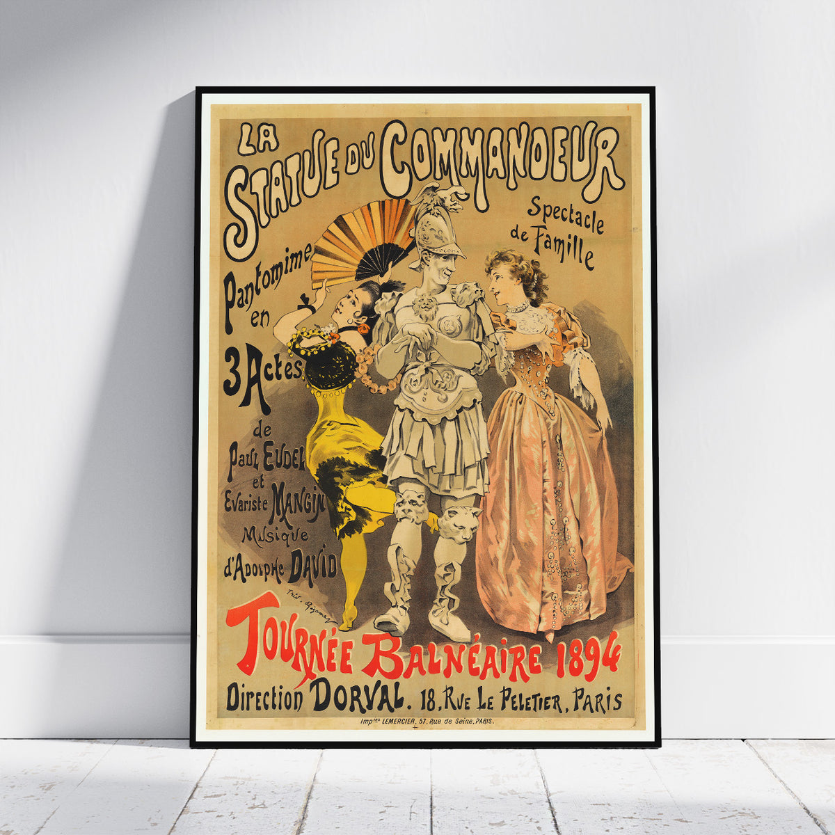 A framed vintage French theatrical poster leaning against a white wall on a light wood floor. The poster features an illustrated performance scene with three figures and ornate typography reading 'La Statue du Commandeur' and 'Tournée Balnéaire 1894'.