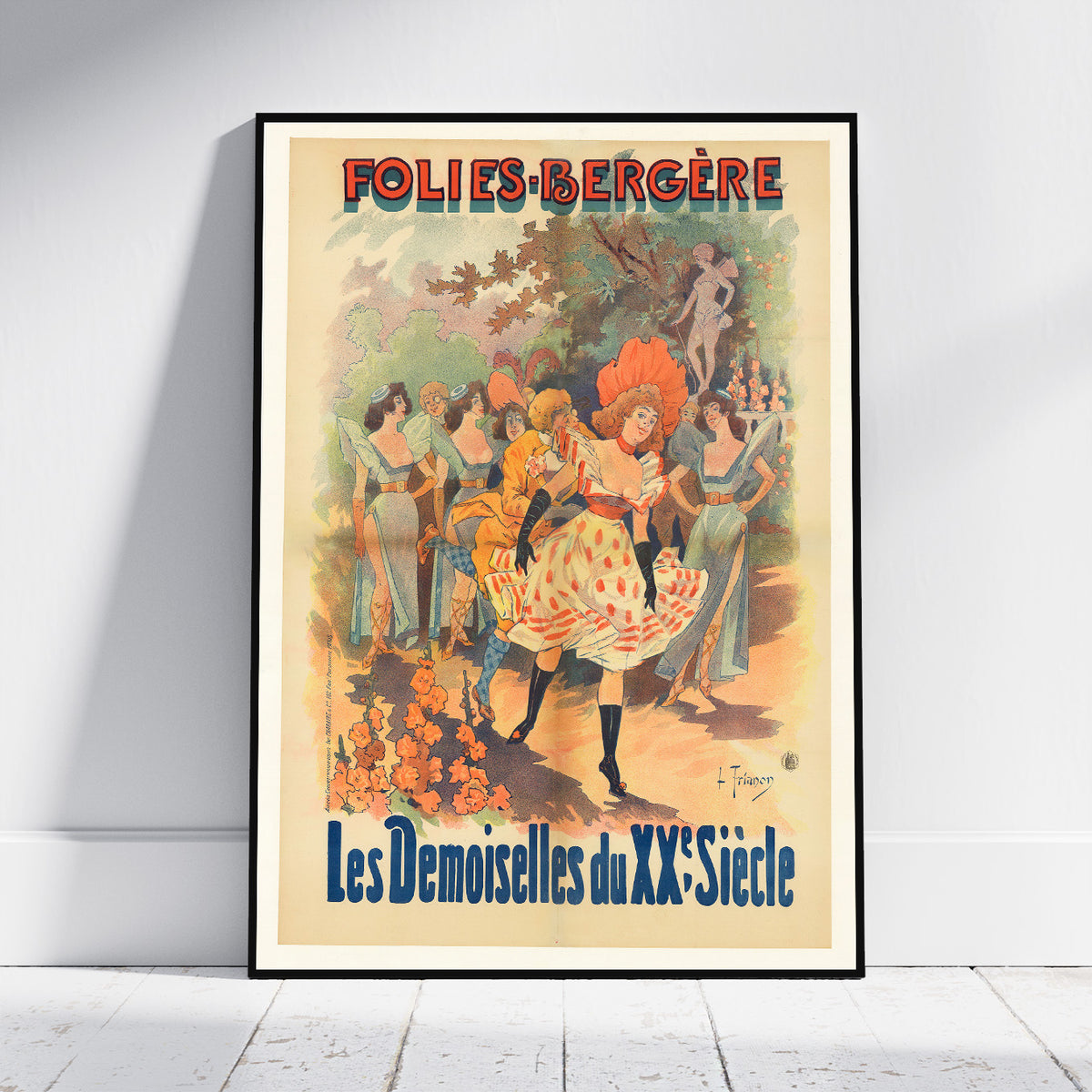 A framed vintage-style poster leaning against a white wall on a light wood floor. The poster features the French text 'FOLIES-BERGÈRE' at the top and 'Les Demoiselles du XXe Siècle' at the bottom, with an illustration of women dancing in an ornate interior scene.