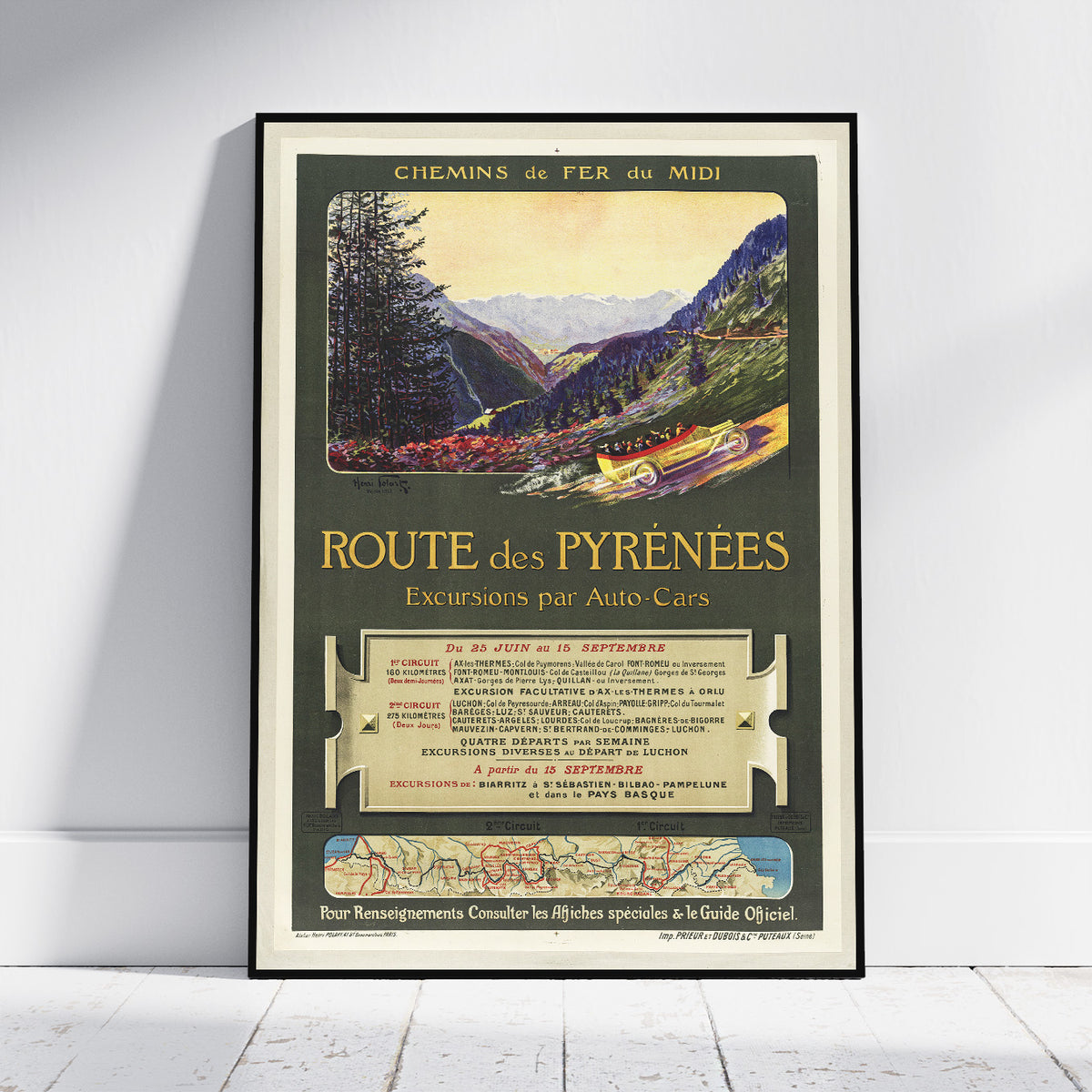A framed vintage travel poster for 'Route des Pyrénées' with an illustration of a mountain valley, early cars, and French text, leaning against a white wall on a light wood floor.