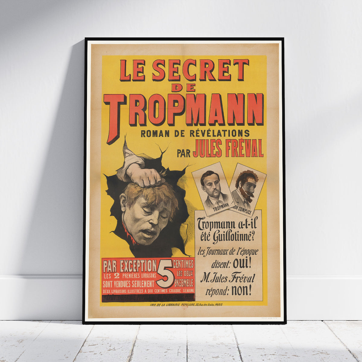A framed vintage French book cover poster for 'Le Secret de Tropmann' by Jules Freval, leaning against a white wall on a light wooden floor.