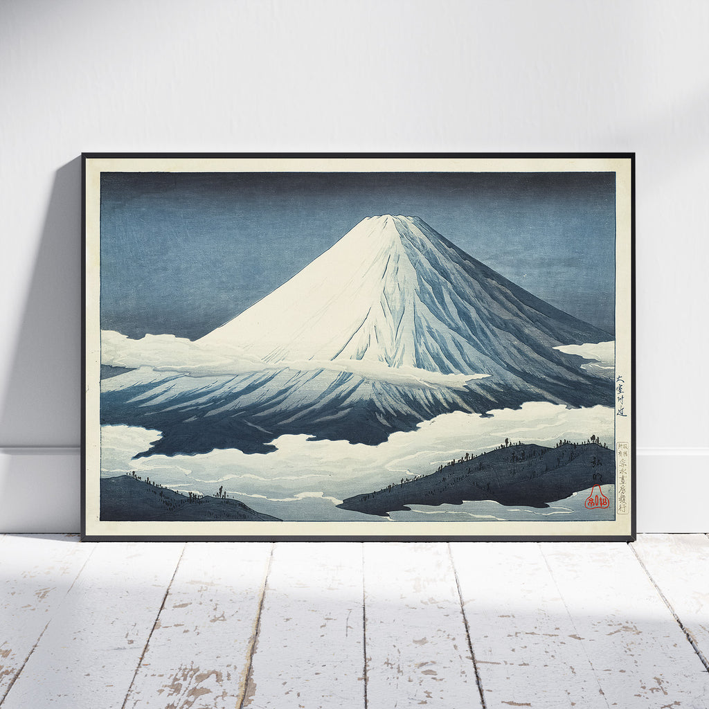 A framed Japanese-style art print of Mount Fuji leaning against a white wall on a white wooden floor. The print features a snow-covered mountain under a dark blue sky, with a black frame and a light beige mat.