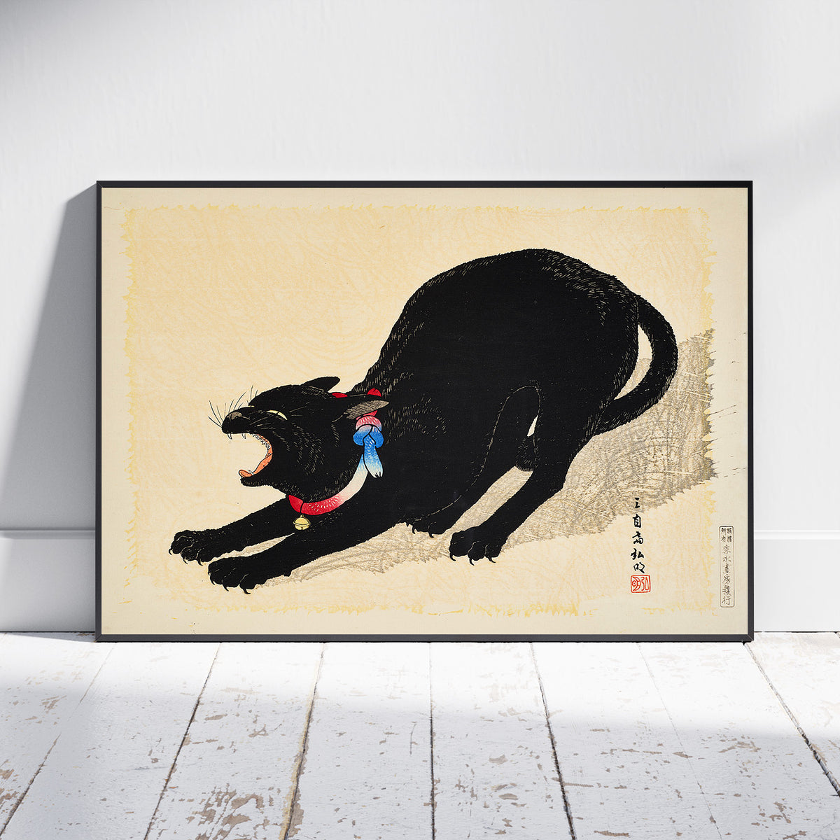 A framed art print depicting a black cat in a dynamic pose with its mouth open, wearing a red collar with a blue bow, set against a cream background. The print is shown leaning against a white wall on a white wooden floor.